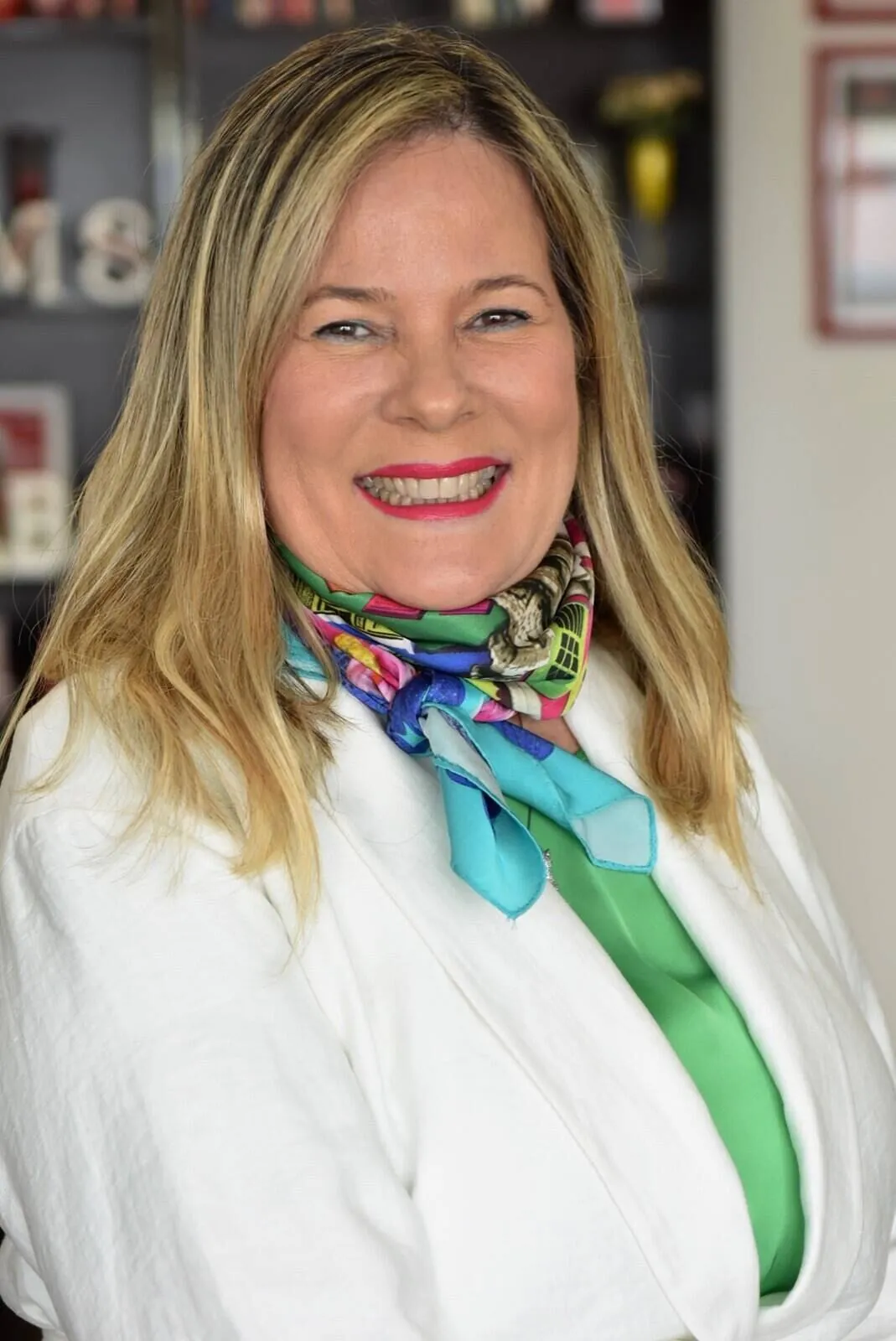 Sandra Martinelli sorrindo, com blazer branco e lenço colorido, em um retrato mais próximo.